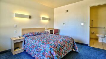Quarto de hotel com cama, mesa de cabeceira, luminária e banheiro com vaso sanitário e pia.