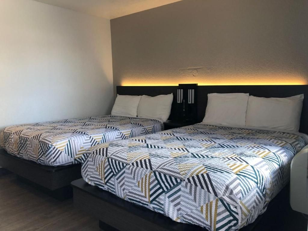 Dos camas con ropa de cama estampada, un cabecero oscuro y una lámpara fijada a la pared.