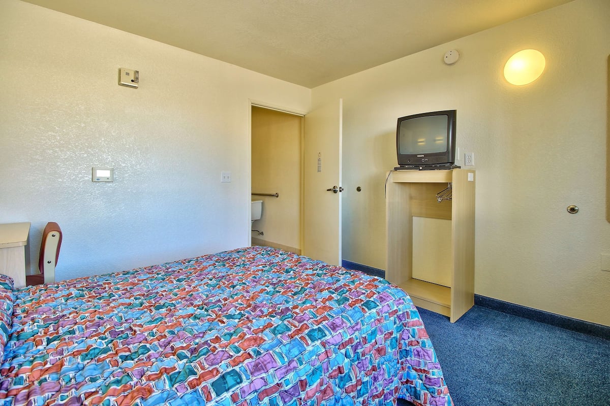 A hotel room with a bed, a television on a stand, a door, and a wall-mounted light.