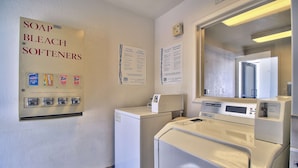 A laundry room with a wall-mounted dispenser for soap, bleach, and softeners. There are instructions for washing and drying, and a coin-operated dryer.