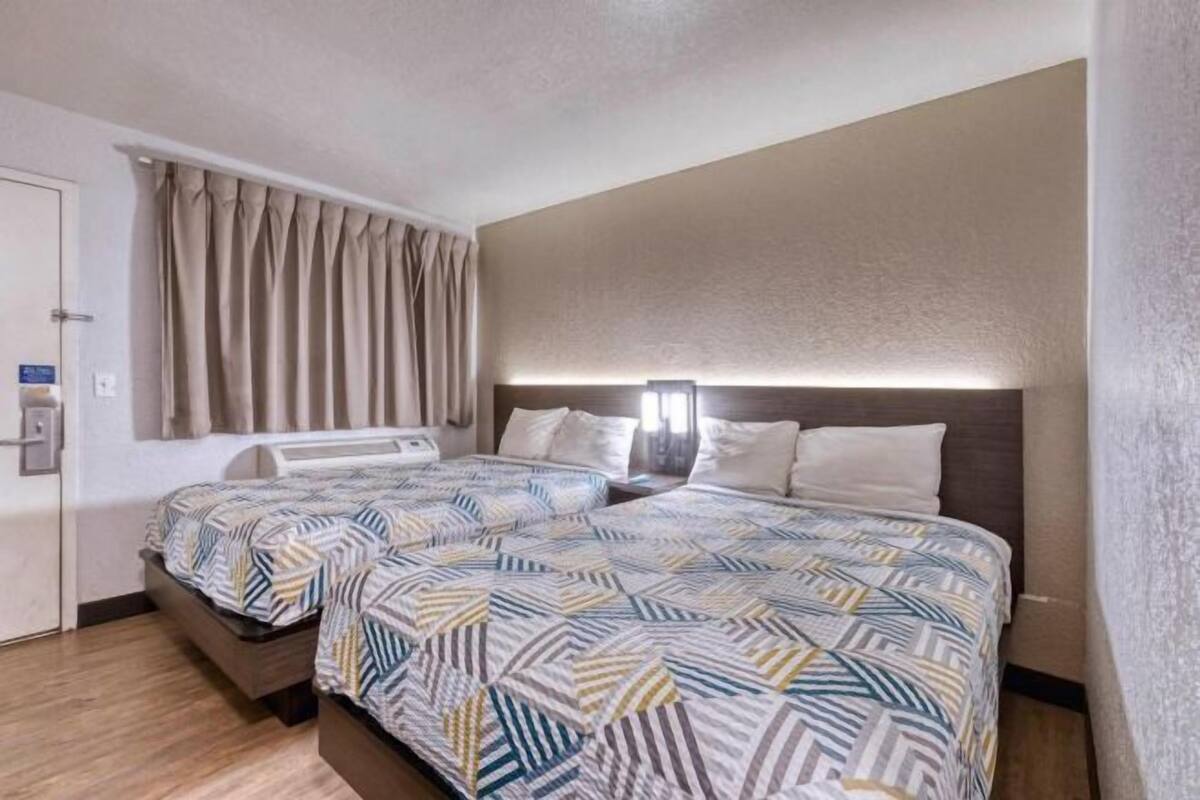 A hotel room with two beds, a headboard, a door, and a curtain.