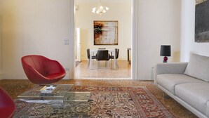A modern living room with a red chair, a grey sofa, a glass coffee table, and a patterned rug.