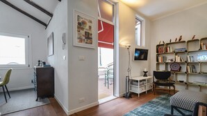 A modern living room with a wooden floor, a bookshelf, a TV, and a dining area with a chair and table. - CA' SVEVA VENICE APARTMENT M0270429660 (Venezia)