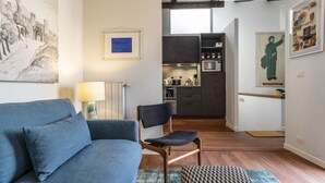 A modern living room with a blue sofa, a wooden chair, and a kitchen in the background. - CA' SVEVA VENICE APARTMENT M0270429660 (Venezia)