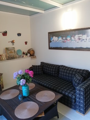 A living room with a patterned sofa, a coffee table with placemats, a wall-mounted picture, and decorative items on shelves. - Newly renovated apartment- studio (Balat Fatih)