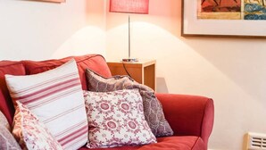 A red sofa with patterned cushions, a floor lamp, and framed artwork on the wall. - Smart flat near Pimlico Tube (London)