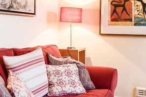 A red sofa with patterned cushions, a floor lamp, and framed artwork on the wall.