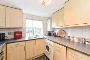 A kitchen with wooden cabinets, a washing machine, a red bread box, and colorful storage containers. - Smart flat near Pimlico Tube (London)