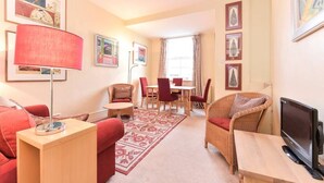A cozy living room with a red sofa, a wooden coffee table, a red armchair, a dining table with chairs, and a flat-screen TV. - Smart flat near Pimlico Tube (London)