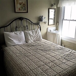 A bed with a patterned bedspread, a nightstand, a wall-mounted mirror, and a window with curtains. - Bath Avenue House (Ocean Grove)
