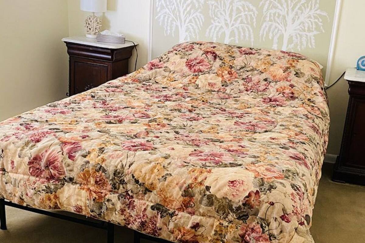 Una cama con una colcha floral, una mesita de noche con una lámpara y una pared decorada con cuadros.