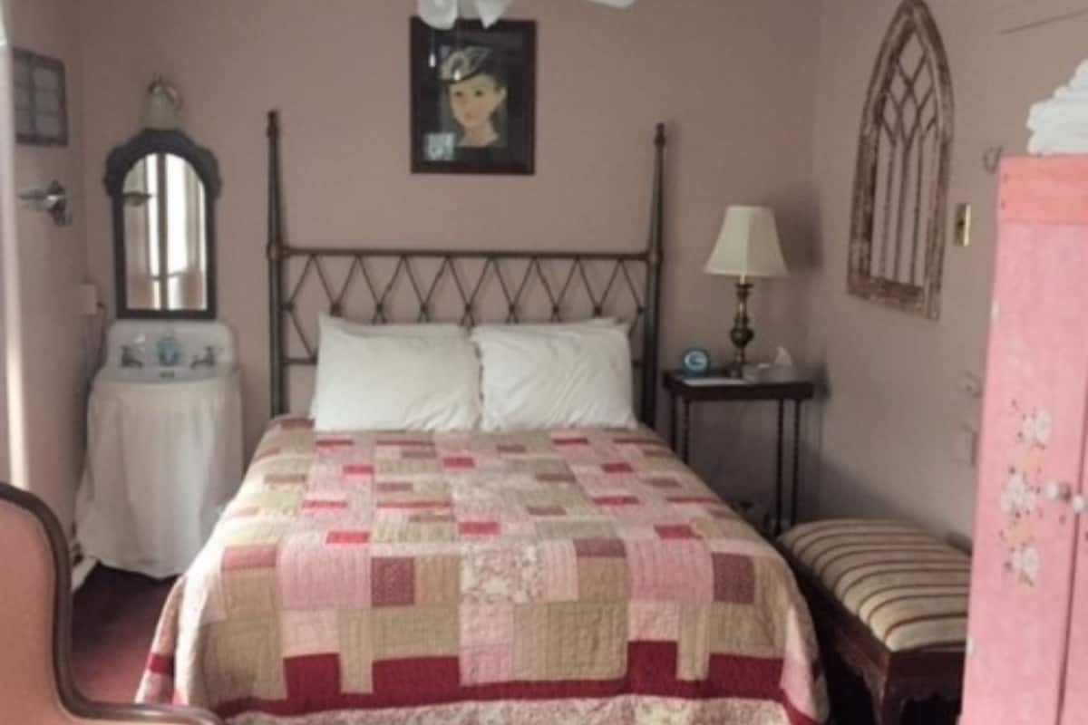 Un dormitorio con una cama, una mesita de noche, una silla, un aparador, un espejo y un ventilador de techo.