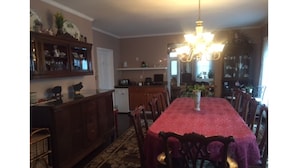 A dining room with a long table covered in a red tablecloth, surrounded by wooden chairs. There is a chandelier hanging above the table. - Bath Avenue House (Ocean Grove)