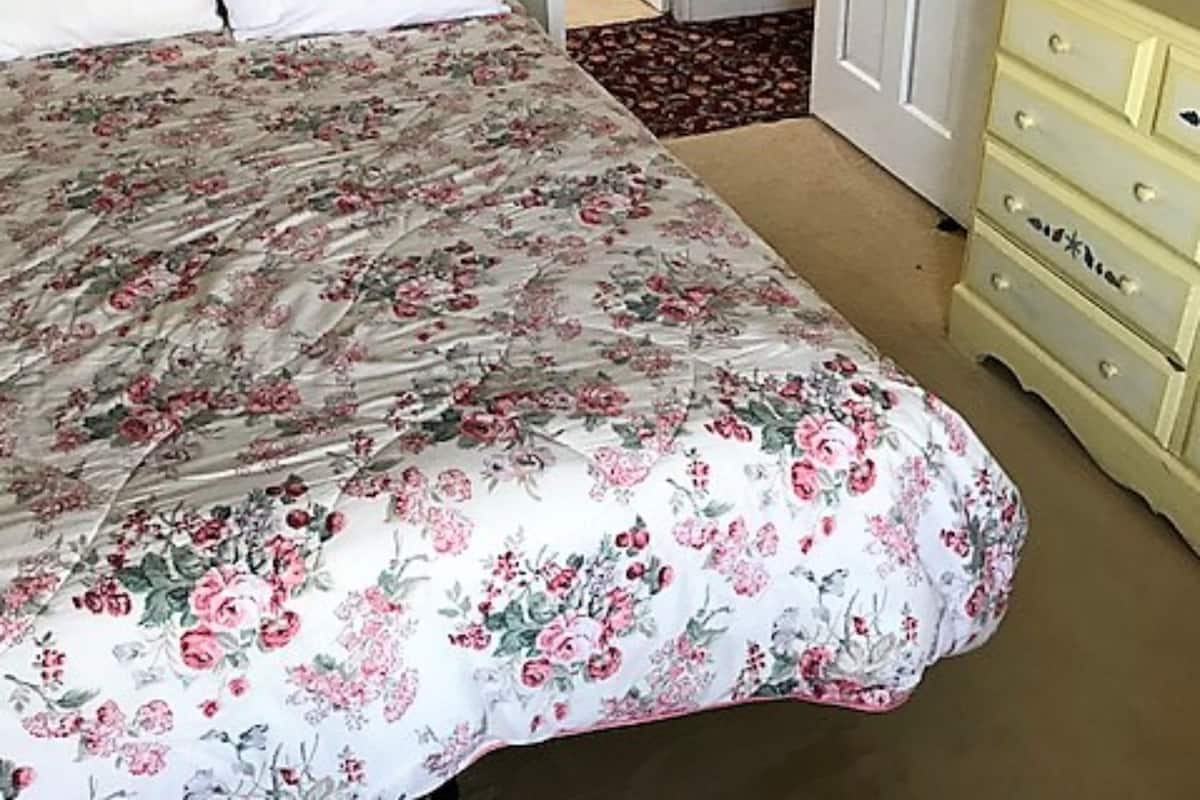 Un dormitorio con colcha floral, cabecero de madera, almohadas blancas y cómoda beige con cajones.