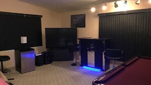 Una habitación con mesa de billar, televisión, zona de bar y área de estar con sofá y sillón.