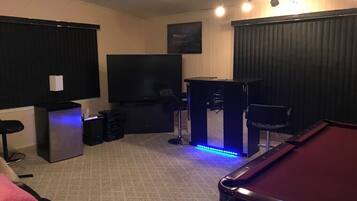 A room with a pool table, a television, a bar area, and a seating area with a couch and a chair.