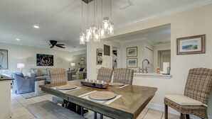 A dining area with a wooden table, wicker chairs, and a hanging light fixture.
