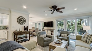 A spacious living room with a ceiling fan, a large clock, and a television.