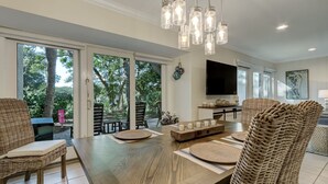 A spacious dining area with a wooden table, wicker chairs, and a modern pendant light fixture.