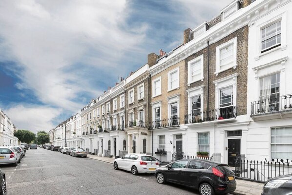 A row of terraced houses with white and brown facades, parked cars, and a clear sky. - Charming flat with balcony in Pimlico (London)