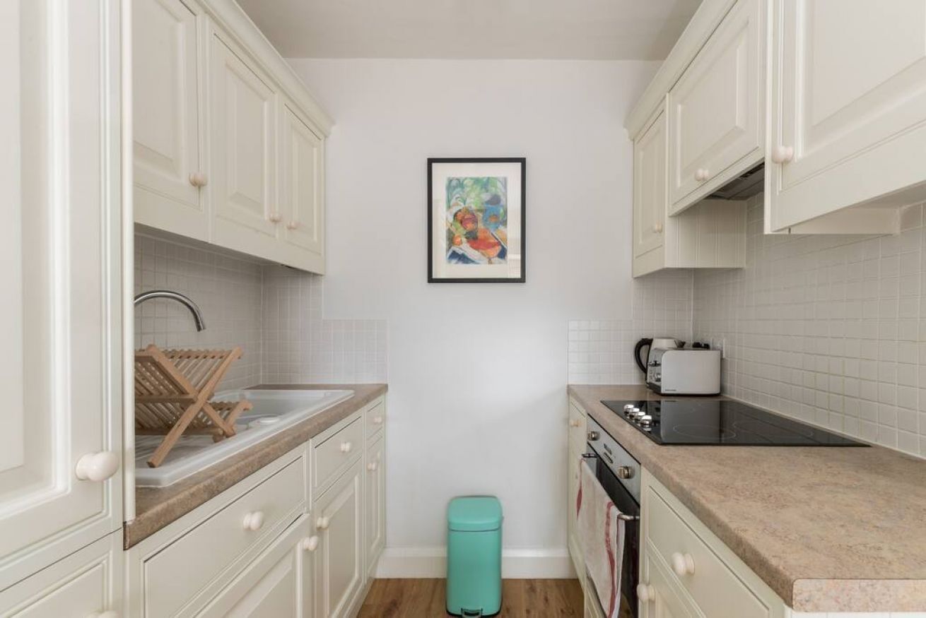 Una cocina compacta con armarios blancos, un lavamanos pequeño, un tostador y un cubo de basura.