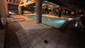 An indoor swimming pool with tiled flooring, lounge chairs, and stone pillars. - Skiing and après ski in pain and residence (Les menuires)