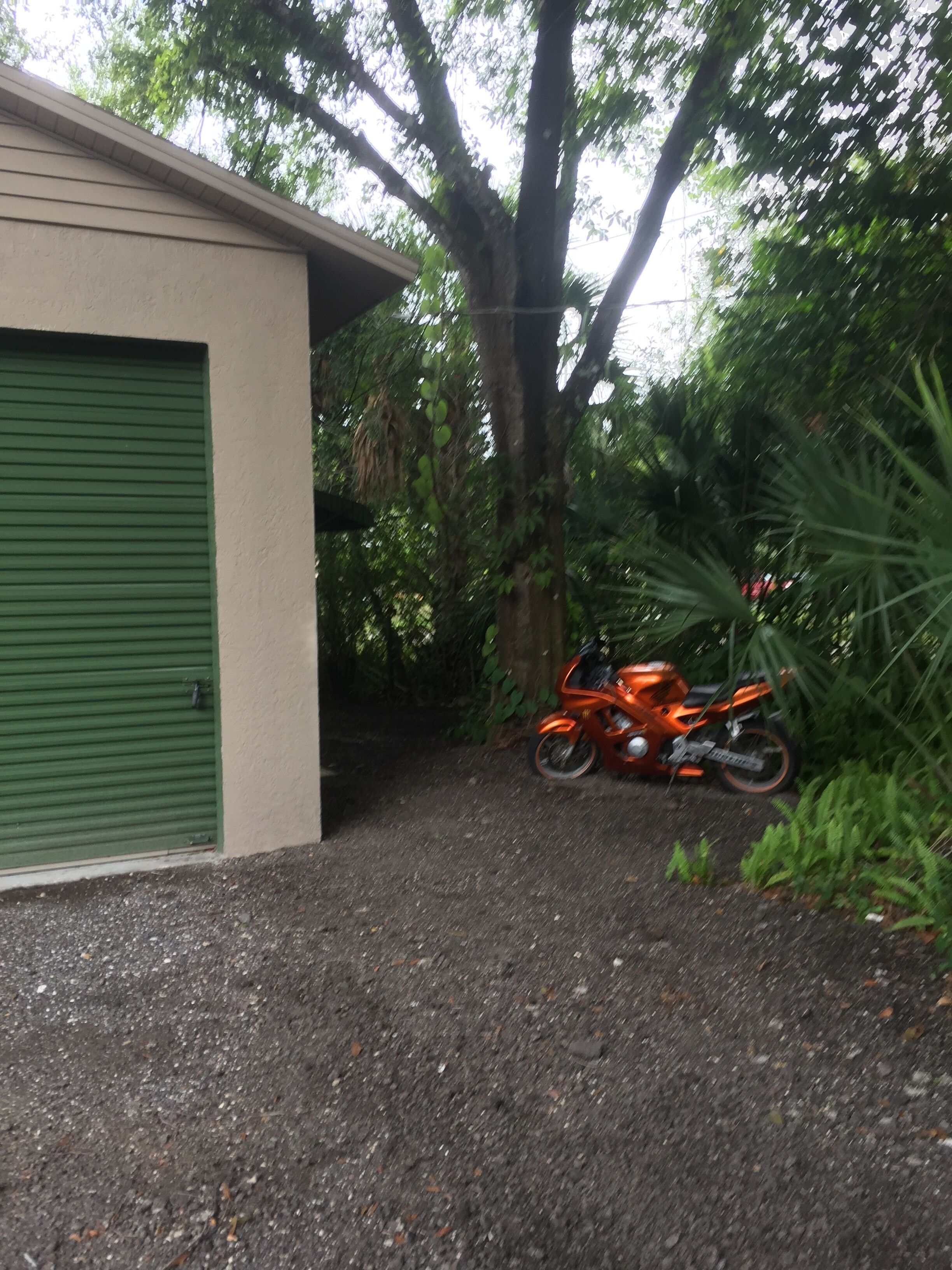 Een gebouw met een groene garage, een grindpad, en een oranje motorfiets ervoor geparkeerd.