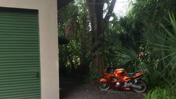 Een gebouw met een groene garage, een grindpad, en een oranje motorfiets ervoor geparkeerd.