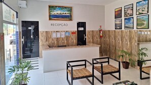 A reception area with a wooden reception desk, framed landscape pictures, and a sign indicating 'RECEPCAO'. - Canto da Duna Hotel (Barreirinhas)