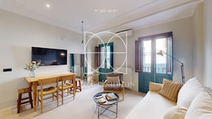 Ein modernes Wohnzimmer mit einem Holzesstisch, einer Couch und einem an der Wand befestigten Fernseher.