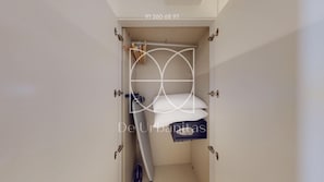 Uma porta estreita que dá para um quarto com uma cama, uma mesinha e uma cadeira.