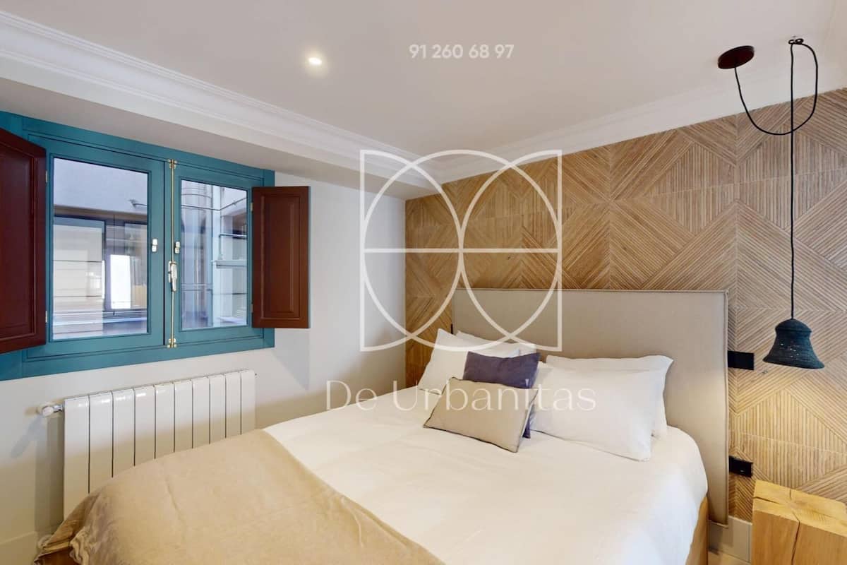 A bedroom with a bed, a window with wooden shutters, a radiator, and a herringbone-patterned wall.
