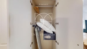 Quarto com cama, mesa de cabeceira e prateleira fixada na parede, com um travesseiro e um controle remoto.