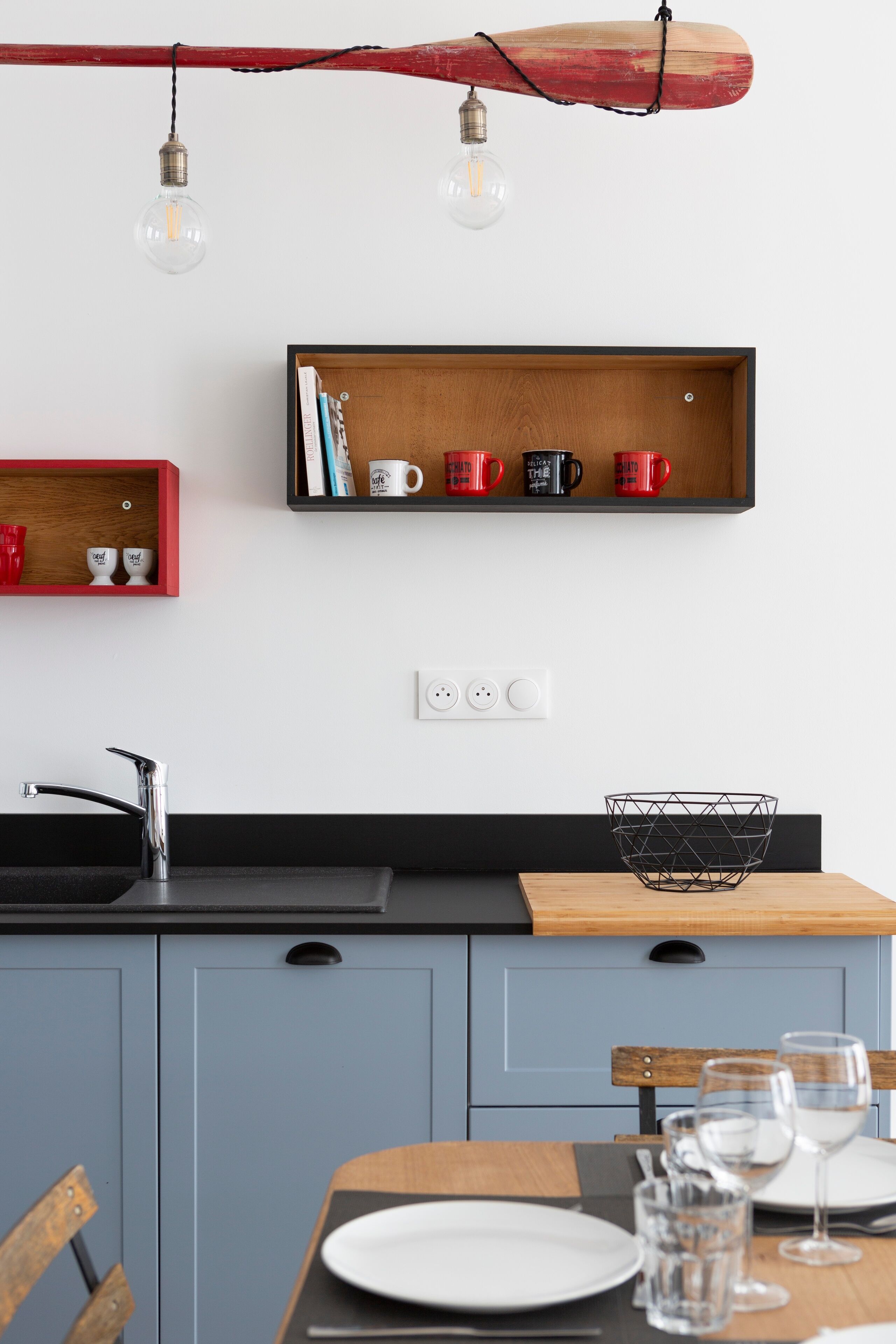 Una cocina moderna con encimera de madera, un lavamanos negro y una zona de comedor con una mesa dispuesta para dos.