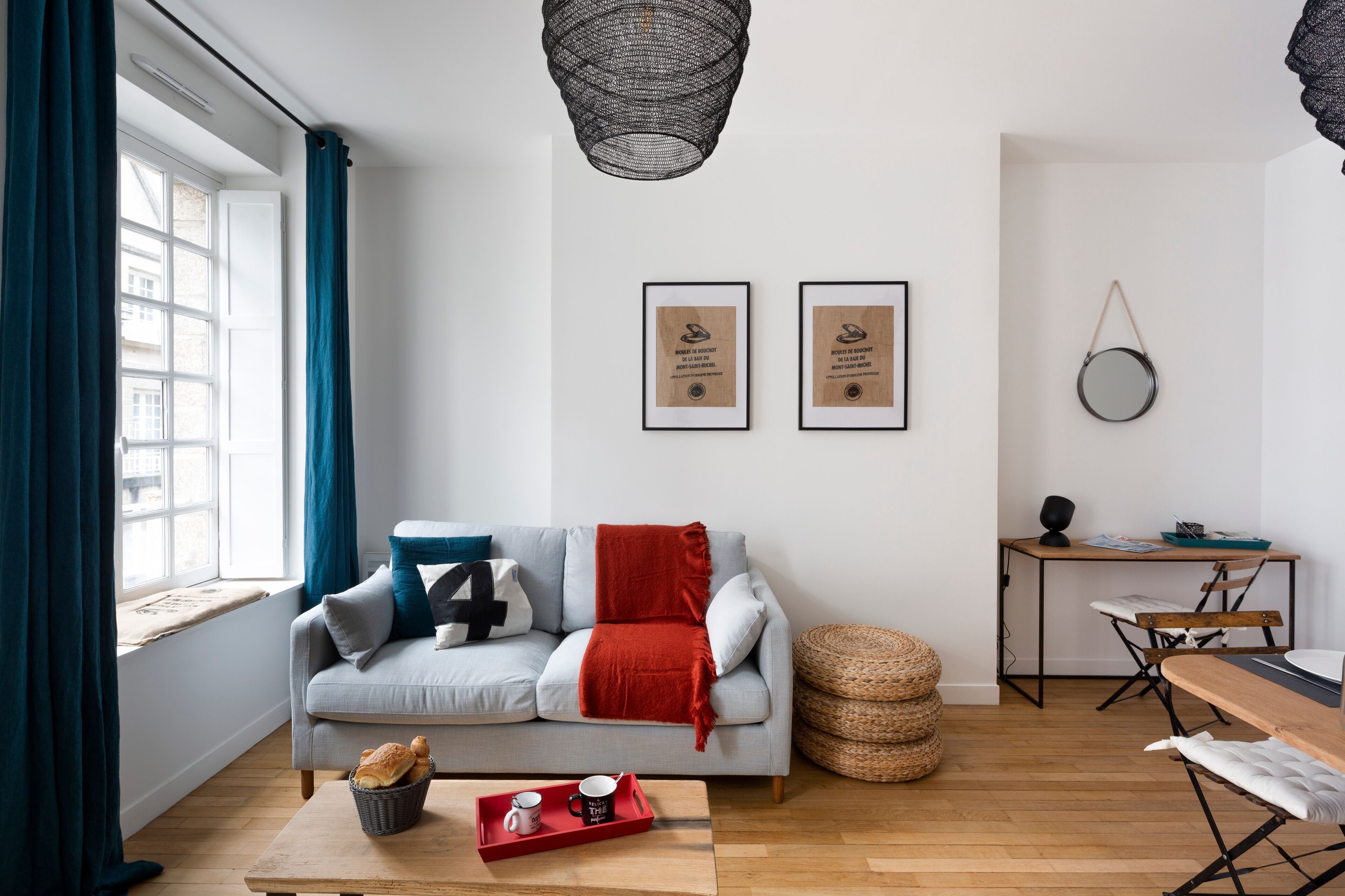Un salon moderne avec un canapé, une table basse et un coin repas. Des certificats encadrés sont accrochés au mur, et un miroir rond est suspendu au-dessus de la table à manger.
