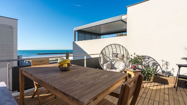 A wooden deck with a table and chairs, a hanging chair, and a view of the ocean. - ARES - Vue Mer - Accès direct plage (Agde)