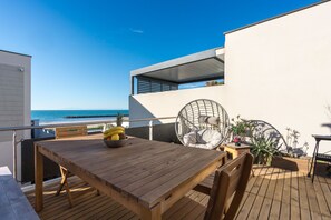 A wooden deck with a table and chairs, a hanging chair, and a view of the ocean.