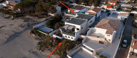 Vista aérea de una zona residencial con casas modernas, una playa arenosa y cielo despejado.