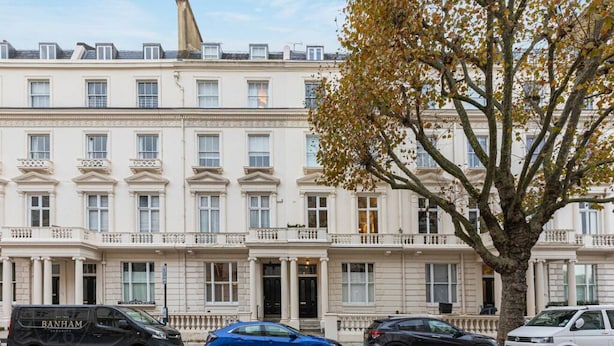 A row of white, classical-style townhouses with a tree in the foreground. - Unique flat near Crescent Garden (London)