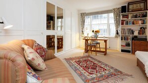A cozy living room with a sofa, a patterned rug, a dining table with chairs, and a bookshelf. - Unique flat near Crescent Garden (London)