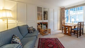 A living room with a sofa, a coffee table, a dining table with chairs, and a window with curtains. - Unique flat near Crescent Garden (London)