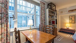 A dining area with a wooden table, chairs, a lamp, and a bookshelf. - Unique flat near Crescent Garden (London)