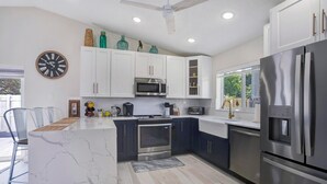 A modern kitchen with white and dark blue cabinets, stainless steel appliances, and a marble island. - Fabulous 3/2 Home in Ft Lauderdale suburb. (Lauderhill)