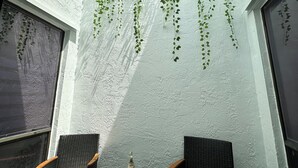 A small outdoor seating area with two wicker chairs and a small table, surrounded by white walls with hanging vines. - Fabulous 3/2 Home in Ft Lauderdale suburb. (Lauderhill)