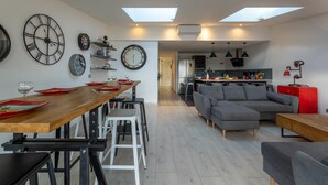 A modern kitchen with a dining area, featuring a wooden table, chairs, and a grey sofa. - VILLA HESTIA - Vue sur la Marina (Agde)