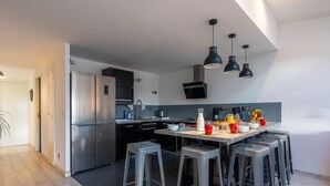A modern kitchen with stainless steel appliances, a central island with stools, and pendant lighting. - VILLA HESTIA - Vue sur la Marina (Agde)