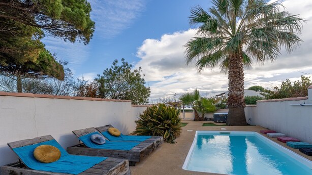 A poolside area with wooden loungers, a palm tree, and a clear blue sky. - VILLA HESTIA - Vue sur la Marina (Agde)