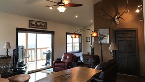 A living room with a ceiling fan, a wooden table, leather chairs, and a door with antlers mounted on the wall.
