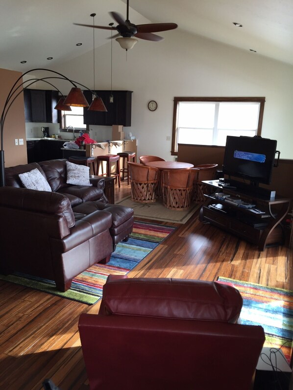 A living room with a brown leather sofa, a red chair, a TV, and a dining area with a table and chairs. - Heart of Paradise Valley (Emigrant)