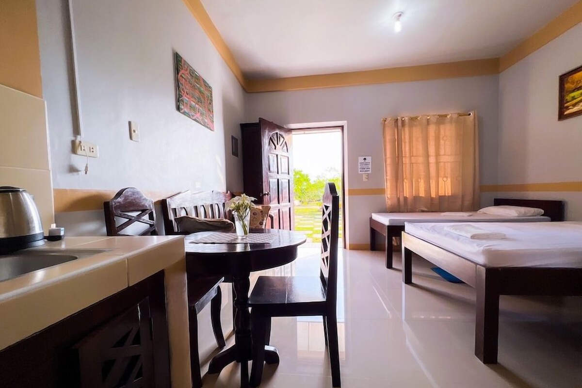 A hotel room with a kitchenette, a dining table with chairs, a bed, and a window with curtains.